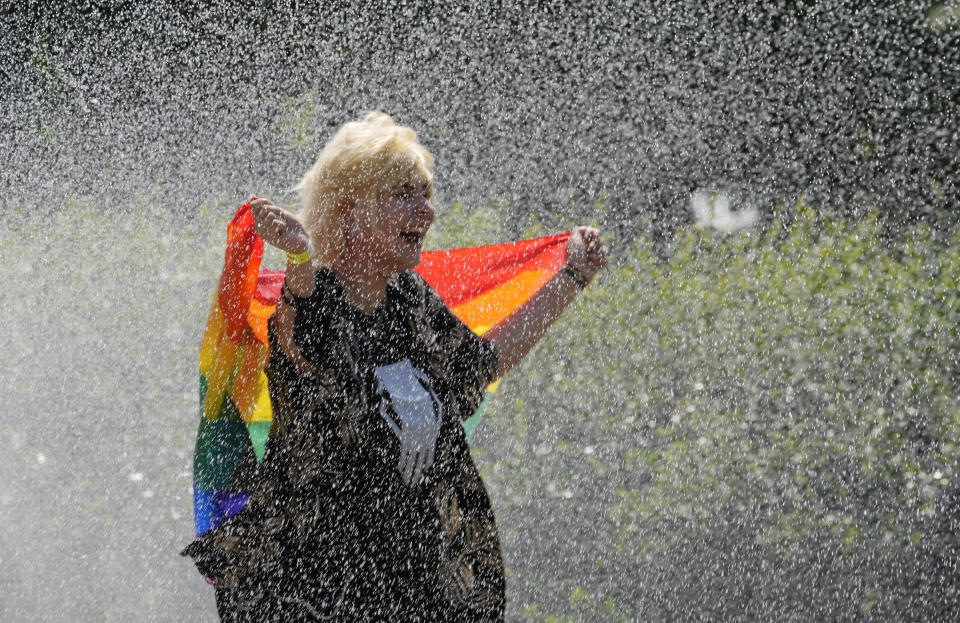 A woman with a rainbow flag cools off in a sprinkler ahead of the Equality Parade, the largest LGBT pride parade in Central and Eastern Europe, in Warsaw, Poland, Saturday, June 19, 2021.(AP Photo/Czarek Sokolowski)