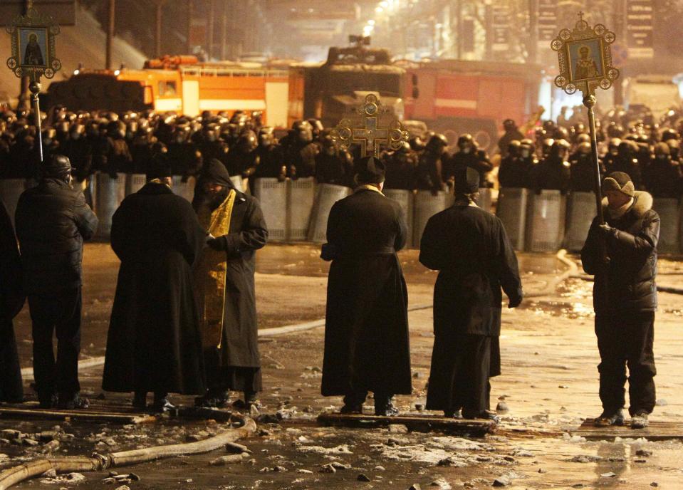 Orthodox priests stand in front of police troops at the site of clashes with anti-government protesters in Kiev