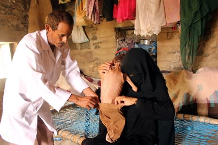 Mother of malnourished Muath Ali Muhammad holds him as a nurse checks him at their home before taking him to a health center in Aslam district of the northwestern province of Hajja