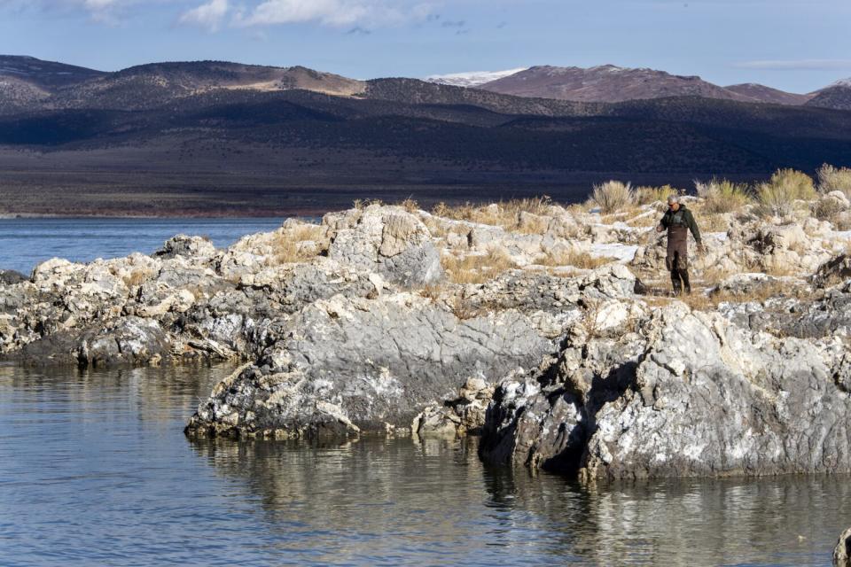 A figure stands on a rocky outcropping on a lake.