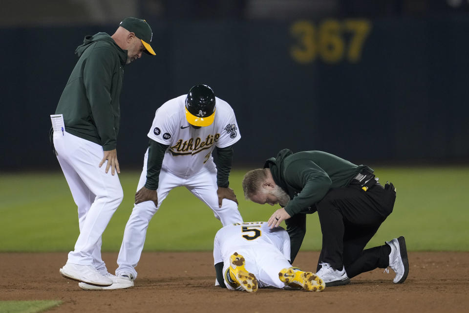 Oakland Athletics' Tony Kemp, bottom, is checked on by manager Mark Kotsay, left, third base coach Eric Martins, middle, and a trainer after reaching second base during the sixth inning of the team's baseball game against the Detroit Tigers in Oakland, Calif., Friday, Sept. 22, 2023. Kemp remained in the game. (AP Photo/Jeff Chiu)