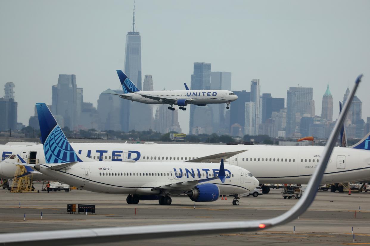 A United Airlines plane lands at Newark Airport, with a widebody and narrowbody in the foreground, and the New York skyline in the background.