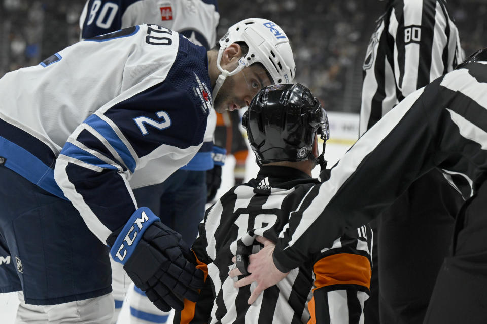 Winnipeg Jets defenseman Dylan DeMelo (2) checks on referee Kyle Rehman, center, after Rahman was hit by a puck during the first period of an NHL hockey game against the Anaheim Ducks in Anaheim, Calif., Thursday, March 23, 2023. (AP Photo/Alex Gallardo)