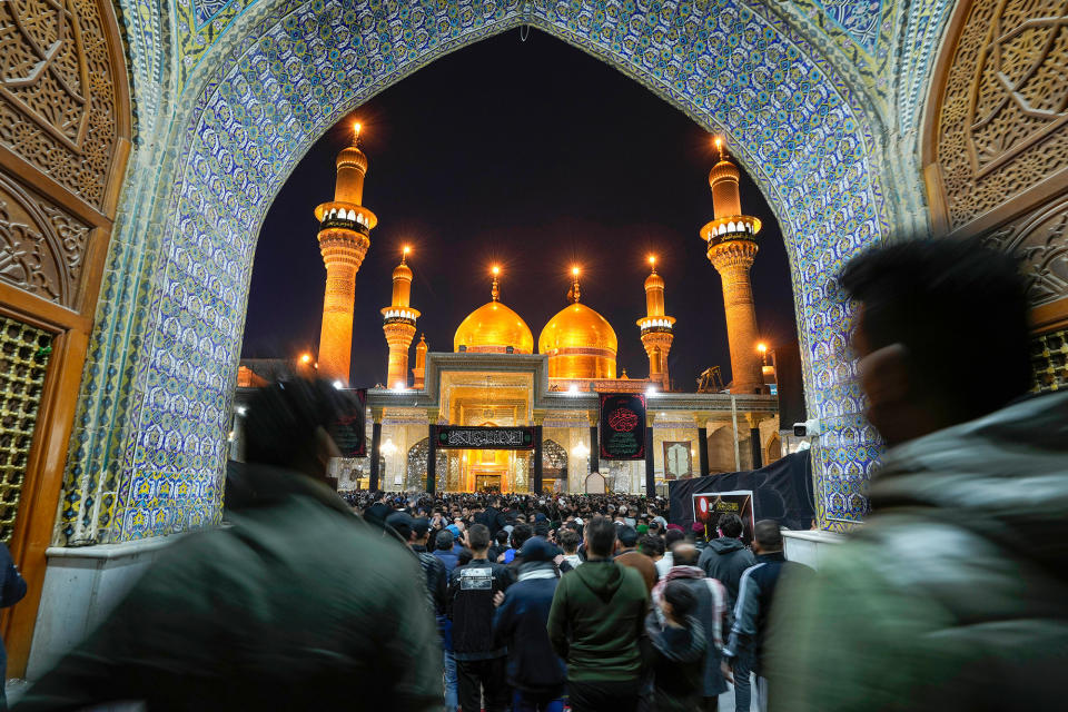 A packed crowd of people look up at the glowing shrine of Imam Moussa al-Kadhim at night