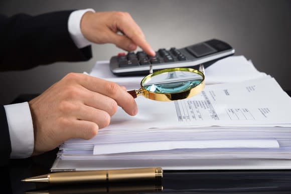 Person in business attire looking through a bill with a magnifying glass and calculator