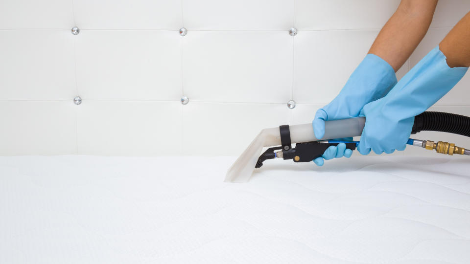 A person wearing blue gloves vacuums the top of a white mattress