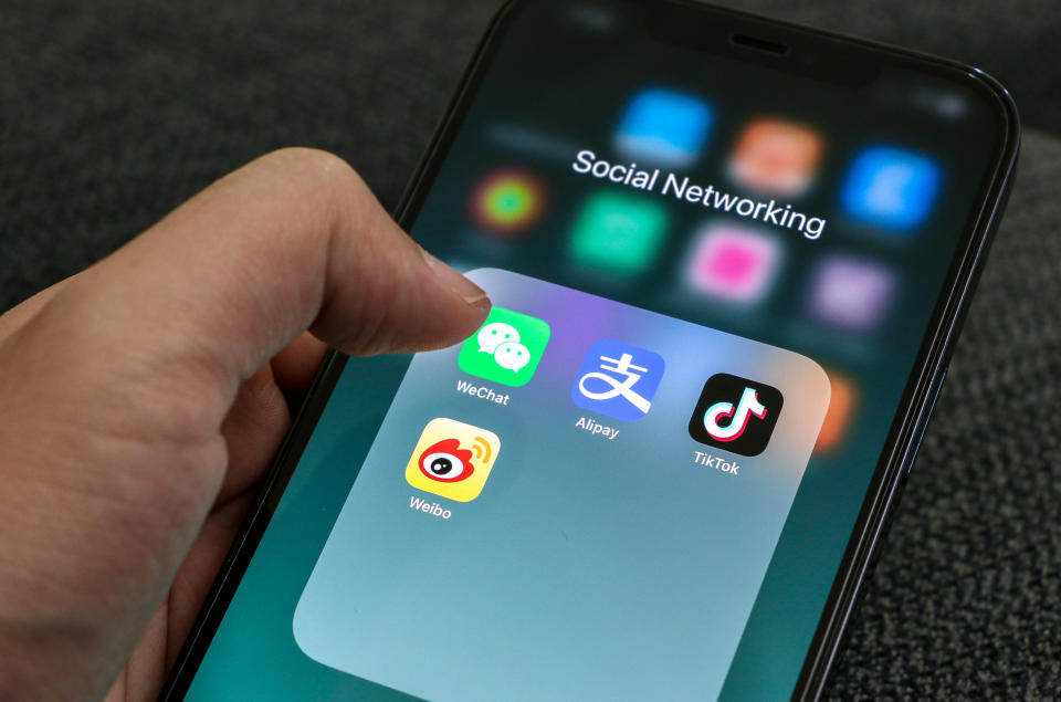 Hand holding a smartphone with thumb clicking on WeChat icon, displayed on screen along with Alipay, Tik Tok and Weibo icons. Social Media concept.