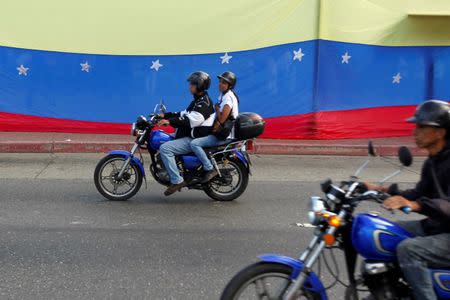 People on motorcycles ride past a Venezuelan National flag, during a rally to demand a referendum to remove Venezuela's President Nicolas Maduro in Caracas, Venezuela, September 1, 2016. REUTERS/Christian Veron