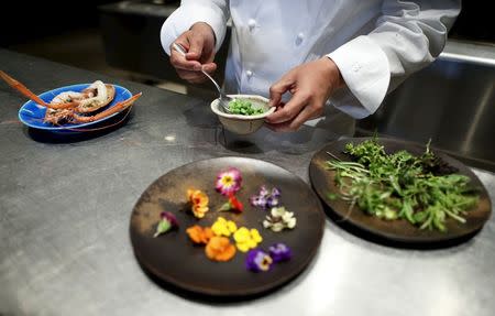 Yoshihiro Narisawa, the owner and chef of Tokyo's French restaurant Narisawa, prepares a dish called "Five flavors", for an early spring menu which includes Akaza Ebi, or langoustine shrimp, from Suruga Bay in central Japan, accented with "green caviar" of various green peas, along with the petals of rucola flowers and viola, at the kitchen of Narisawa in Tokyo March 26, 2015. REUTERS/Yuya Shino