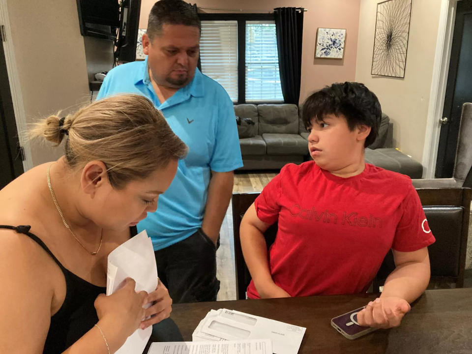  Antonio Arellano (center) watches as his wife, Abigail, and son, 11-year-old Samuel, go through the many medical bills the family received after Samuel was shot at the Kansas City Chiefs Super Bowl parade on Feb. 14, 2024. (Peggy Lowe/KCUR 89.3)
