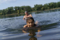 Anastasiia Aleksandrova, 12, plays in the water while swimming with her grandfather, Andreii, rear, at a lake in Sloviansk, Donetsk region, eastern Ukraine, Monday, Aug. 8, 2022. The mass displacement of Ukrainians, overwhelmingly women and children, has upended countless childhoods, not only for those having to start a new life after seeking safety elsewhere, but also for the thousands who have stayed behind. (AP Photo/David Goldman)