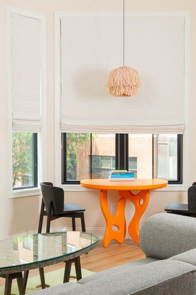 A fluffy Llot Lov pendant hangs above a custom neon-orange Paradise Grey dining table. The chairs are by Blu Dot. Atop a Bi-Rite rug is a coffee table by local arts non-profit Rair made entirely of upcycled materials. The muted gray sofa is by Audo.