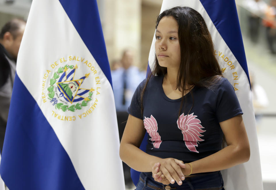 Tania Vanessa Avalos stands nearby as a government official speaks at a press conference at the airport, after her arrival in San Salvador, El Salvador, Friday, June 28, 2019. Avalos is the wife of the young man who drowned alongside his 23-month-old daughter while trying to cross the Rio Grande into Texas on Sunday, June 23. (AP Photo/Salvador Melendez)
