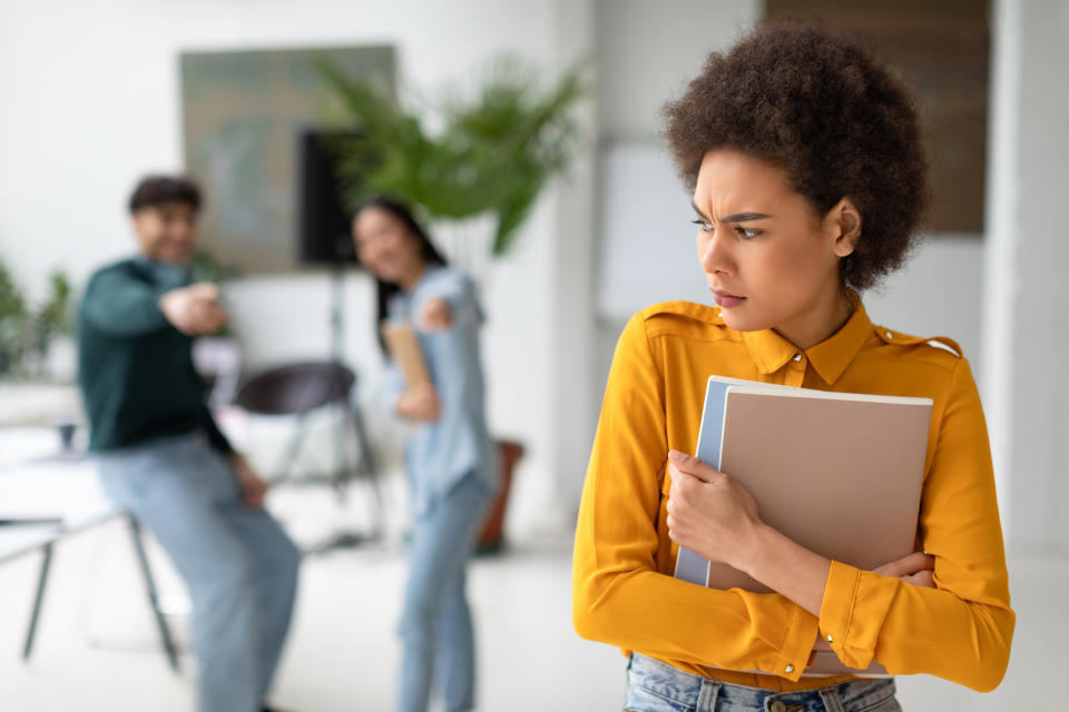 Woman looks uncomfortable while a couple points at her accusingly in a room