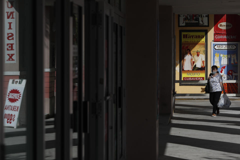 FILE- In this Oct. 28, 2020, file photo, a woman walks past store publicity on Calle Ocho in the Little Havana section of Miami. Defying fears of another slowdown, U.S. businesses kept hiring at a solid pace in October yet there are signs they remain cautious about the economy's future as the pandemic worsens. (AP Photo/Rebecca Blackwell, File)