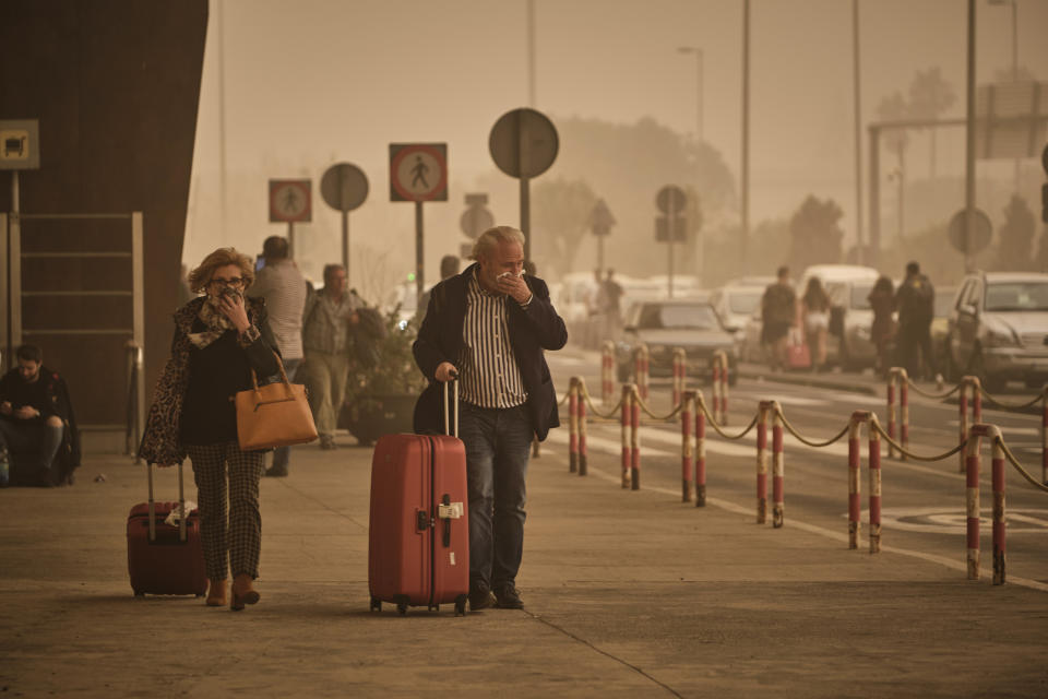 Two passengers cover their noses and mouths in a cloud of red dust at the airport in Santa Cruz de Tenerife, Spain, Sunday, Feb. 23, 2020. Flights leaving Tenerife have been affected after storms of red sand from Africa's Saharan desert hit the Canary Islands. (AP Photo/Andres Gutierrez)