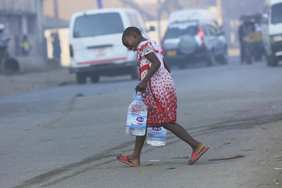 A girl crosses a busy road while carrying water containers in Harare, Friday, 9, 2019. Fuel prices and the general cost of living continue to rise in Zimbabwe as the public struggle against basic shortages of water and power. (AP Photo/Tsvangirayi Mukwazhi)