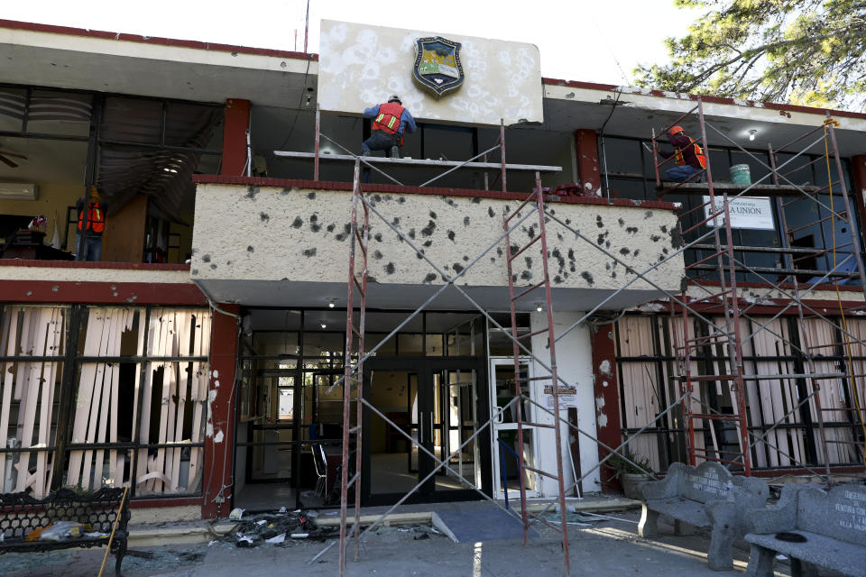 Workers repair the facade of City Hall riddled with bullet holes, in Villa Union, Mexico, Monday, Dec. 2, 2019. The small town near the U.S.-Mexico border began cleaning up Monday even as fear persisted after 22 people were killed in a weekend gun battle between a heavily armed drug cartel assault group and security forces. (AP Photo/Eduardo Verdugo)