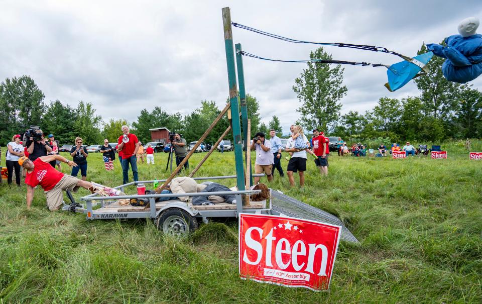 (Left) Matthew Allan of Burlington, uses the slingshot he built for the Adam Steen rally where they hosted a toss Speaker Robin Vos using a bungee slingshot and a Vos dummy on Monday August 8, 2022 in Burlington, Wis.