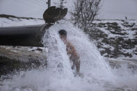 An Israeli man sits under hot water coming out of a pipe from a drilling project which exposed a subterranean hydrothermal spring, at a snow-covered reservoir next to Mount Bental in the Israeli-controlled Golan Heights, near the Israeli border with Syria Wednesday, Jan. 19, 2022. Snow fell in parts of the Middle East as a winter storm swept through the region. (AP Photo/Ariel Schalit)