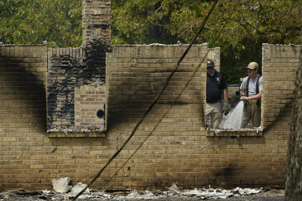 A member of the Mississippi State Fire Marshal's Office, left, waits as a firefighter waters down hot spots inside a burned out house, Wednesday morning, April 26, 2023, in Conway, Miss. Authorities believe a man who escaped from a Mississippi jail over the weekend with three others, and is suspected of killing a pastor, is believed to be dead after a shootout with authorities and barricaded himself inside a burning home near Conway, Mississippi. (AP Photo/Rogelio V. Solis)