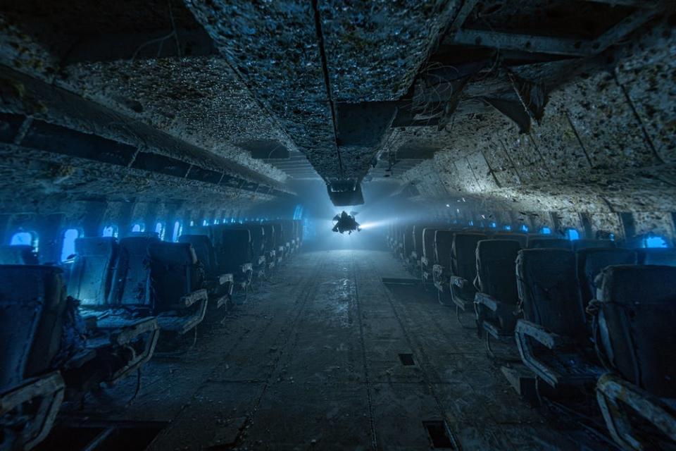 A lone diver floats at the end of a submerged Lockheed TriStar L-1011 passenger plane in the Red Sea off Jordan's coast, the rows of seats visible either side. The image is a winner in the 2024 Underwater Photographer of the Year Awards.