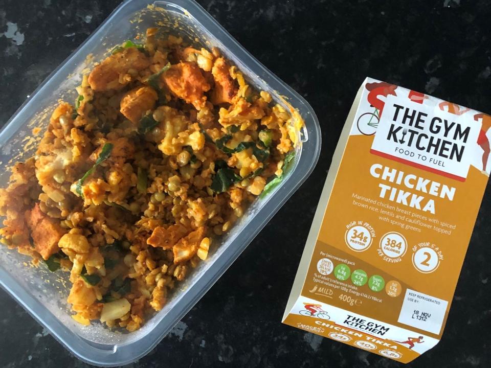 Plastic container of chicken tikka dish next to a box with "The Gym Kitchen" and "Chicken Tikka" on it