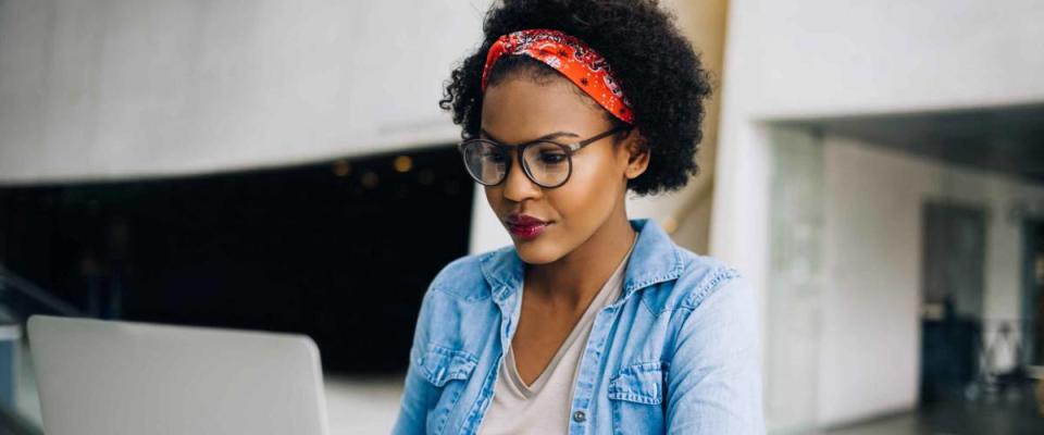 Smiling young African female entrepreneur hard at work on a laptop while sitting at a table in the lobby of a modern office building