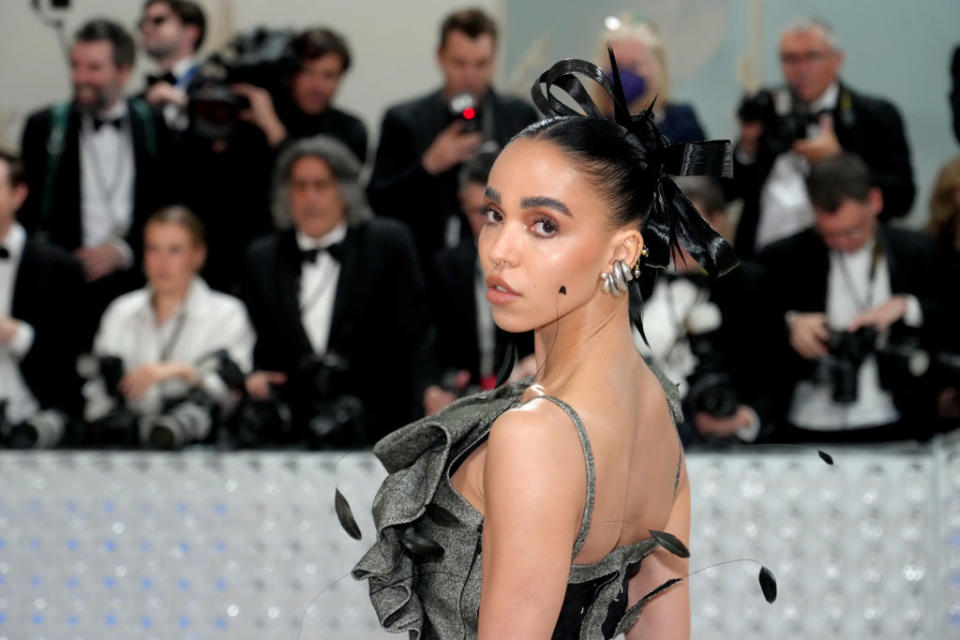 FKA in an elegant gown with a bow on her head, photographers in the background