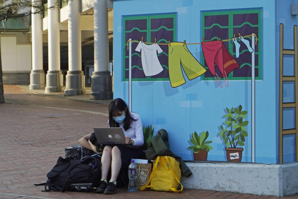 A woman wearing a face mask to help curb the spread of the coronavirus, uses her computer on a street in Hong Kong, Monday, Nov. 30, 2020. (AP Photo/Kin Cheung)