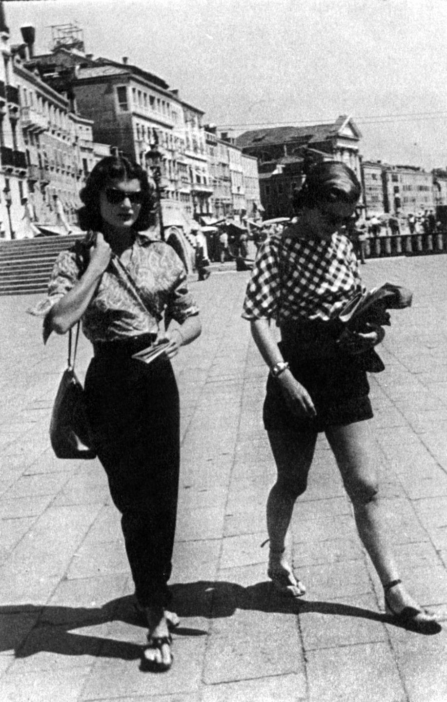 <p>Sisters Jacqueline and Caroline Lee Bouvier play the part of chic locals while traveling in Venice. Jackie wears a paisley-printed blouse with black paper-bag pants. <br></p>