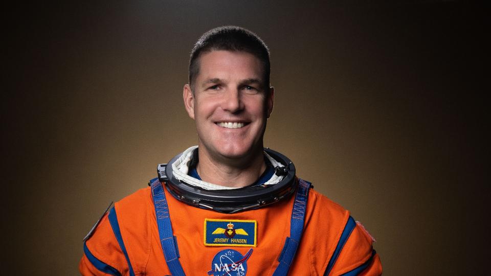 an astronaut smiles for a portrait in an orange spacesuit