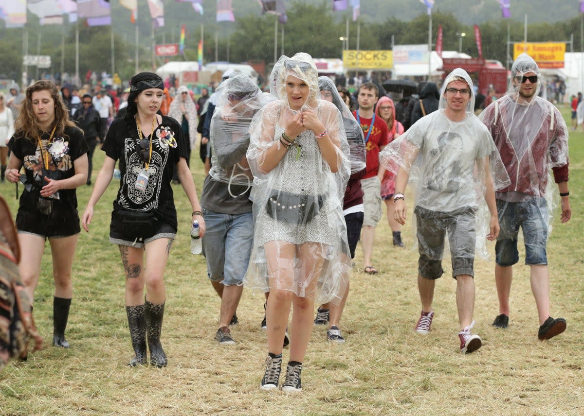 Festival goers during a rain shower at the Glastonbury Festival (PA) (PA Archive)