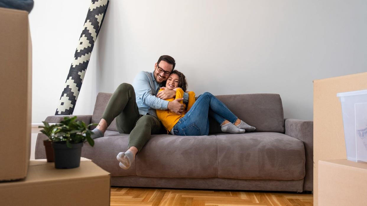 Husband and wife surrounded by cardboard boxes excited to move in new own house apartment.