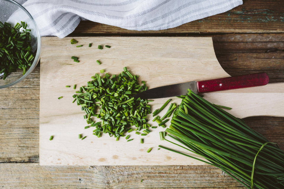 Chopped and whole chives and kitchen knife on wooden board