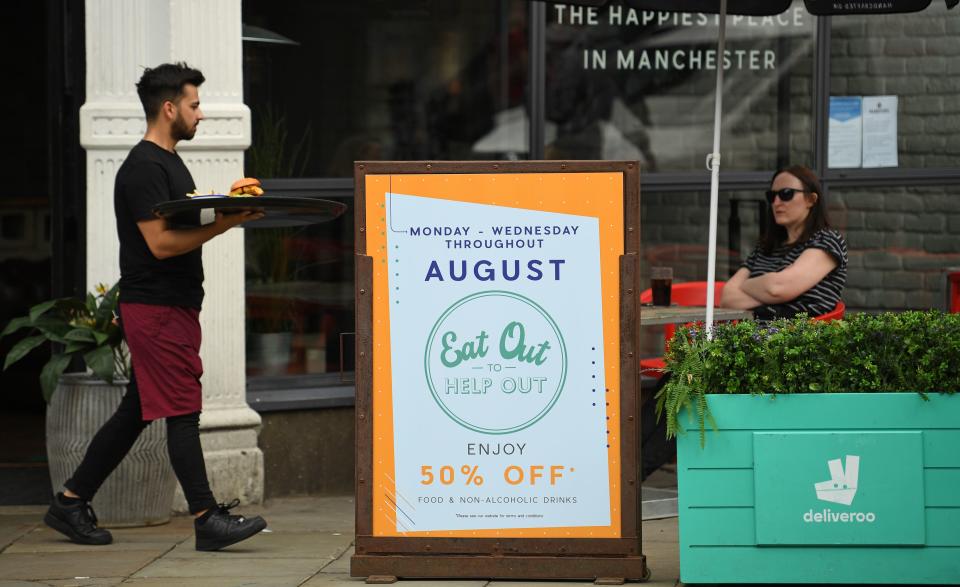 A server carries food past a sign promoting the British Government's "Eat out to Help out" COVID-19 scheme to get consumers spending again, outside a restaurant in Manchester, northwest England on August 3, 2020. - Britain's "Eat out to Help out" scheme began Monday, introduced last month by Chancellor Rishi Sunak to help boost the economy claw its way from a historic decline sparked by the coronavirus crisis. (Photo by Oli SCARFF / AFP) (Photo by OLI SCARFF/AFP via Getty Images)