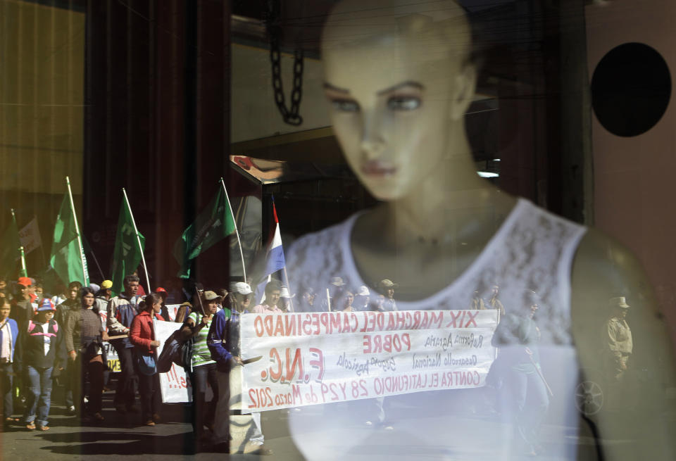 FILE - In this March 29, 2012 file photo, farmers are reflected in a storefront window as they make their way to the Plaza de Armas as part of the annual National Farmers Federation march to demand land reforms in Asuncion, Paraguay. The roots of Paraguay's land crisis stretch back 140 years, through a seemingly intractable pattern that keeps about 1 percent of the population in control of 77 percent of arable land while 31 percent of Paraguayans live in extreme poverty, according to the United Nations. (AP Photo/Jorge Saenz, File)