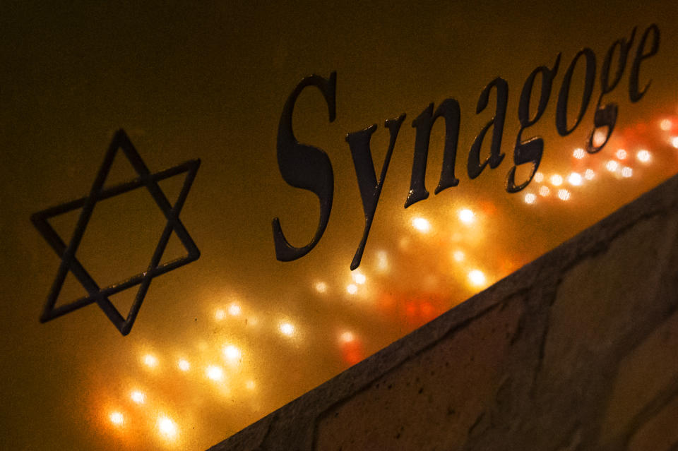 FILE - In this Friday, Oct. 11, 2019 file photo, candles reflect in an entrance sign after a human chain with lights was formed around the Jewish synagogue during the Sabbath celebrations in Halle (Saale), Germany, following an attack on the synagogue on Yom Kippur 2019. As Jews around the world gather Sunday night to mark the beginning of Yom Kippur, many in Germany remain uneasy about going together to their houses of worship to pray, a year after a white-supremacist targeted a synagogue in the eastern city of Halle on the holiest day in Judaism. (AP Photo/Jens Meyer, file)