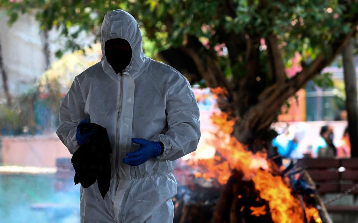 A relative wearing PPE stands in front of the cremation pyre of a person who died from the COVID-19