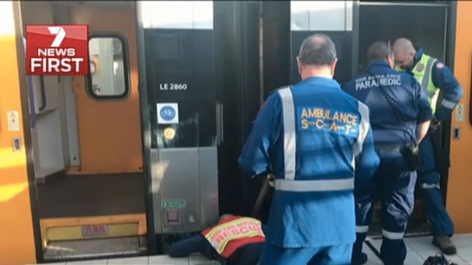 A NSW Fire and Rescue worker reaches below the platform in what was a 40 minute process to remove the trapped woman. Source: 7 News