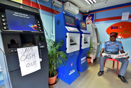 A security guard reads a newspaper inside an ATM counter as a notice is displayed on an ATM in Guwahati, India, November 27, 2016. REUTERS/Anuwar Hazarika