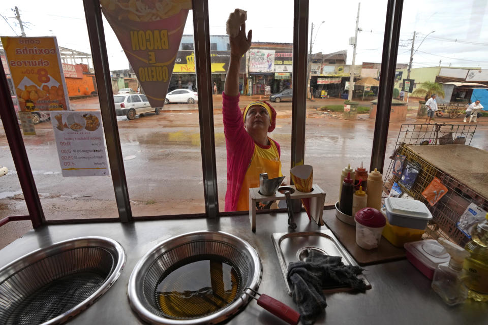 Francisca Celia cleans the glass of her cart where she sells chips, on the main street of the Sol Nascente favela of Brasilia, Brazil, Monday, March 20, 2023. Celia said residents still need basic sanitation and infrastructure but that available plots of land are much bigger than in other favelas in Rio and that it isn’t nearly as disorganized or dangerous. (AP Photo/Eraldo Peres)
