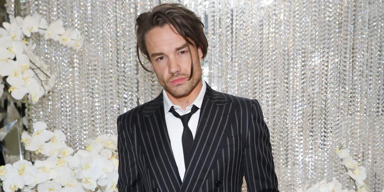 liam payne in june 2023 wearing a black and grey pinstriped suit standing in front of white flowers, a wall of hanging crystal beads, and a white neon sign that reads annabels 60th birthday