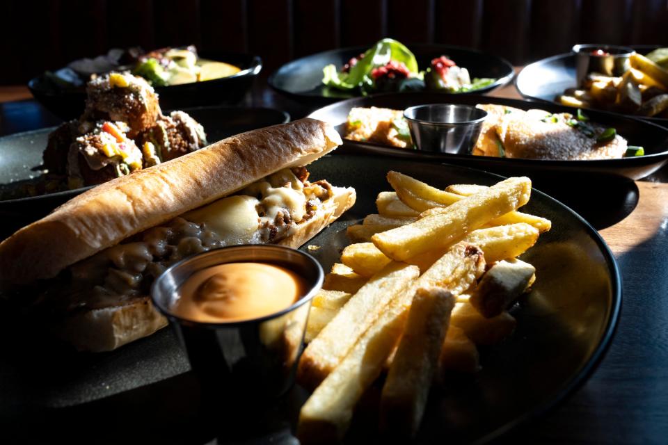 Feb 21, 2023; Columbus, Ohio, United States;  Sunlight falls onto a bulgogi cheesesteak sandwich, veggie burger, kimchi pancakes, elote fritters and a shaved veggie salad at Columbus Brewing Company’s newly opened beer hall in Franklin Park. Mandatory Credit: Joseph Scheller-The Columbus Dispatch