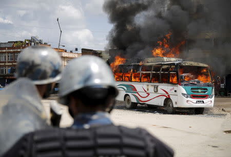 Police stand in front of a burning passenger bus after it was set on fire by unidentified protesters during the nationwide strike, called by the opposition parties against the proposed constitution, in Kathmandu, Nepal September 20, 2015. REUTERS/Navesh Chitrakar