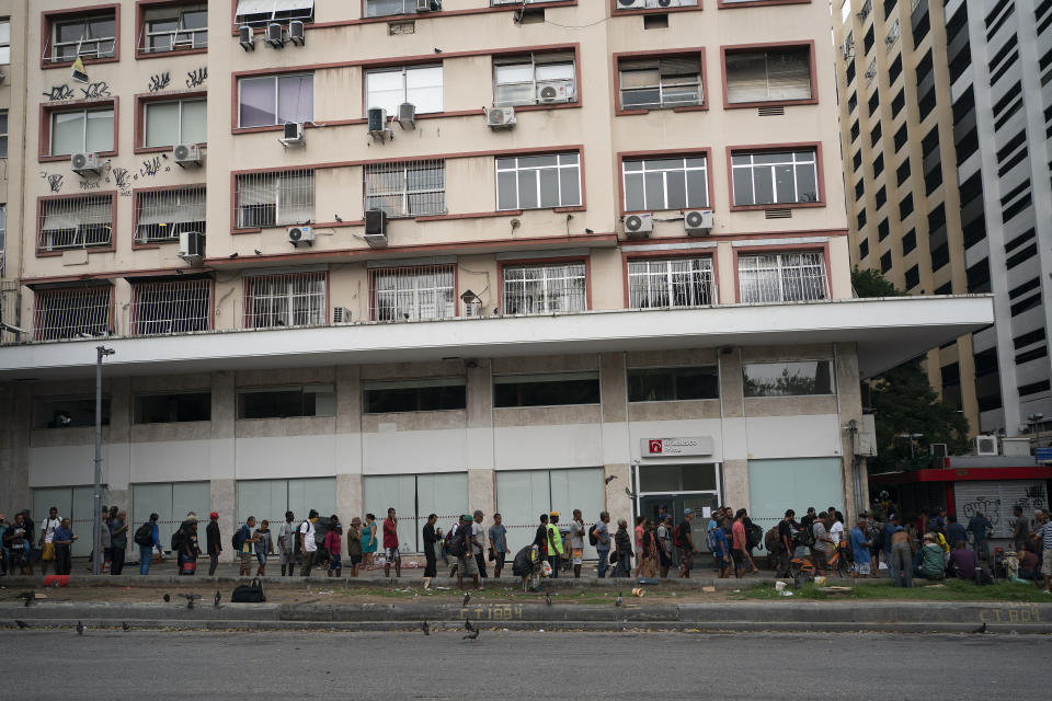 Homeless people wait in line for a cup of coffee and bread from a private charity in downtown in Rio de Janeiro, Brazil, Monday, March 30, 2020, while most other residents are staying home to help contain the spread of the new coronavirus. (AP Photo/Leo Correa)