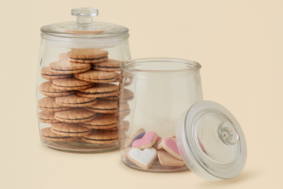 2 BIG W clear glass cookie jars filled with cookies on a beige background