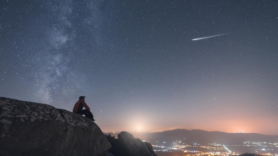 A man looks at a shooting star, the Milky Way and the moon setting