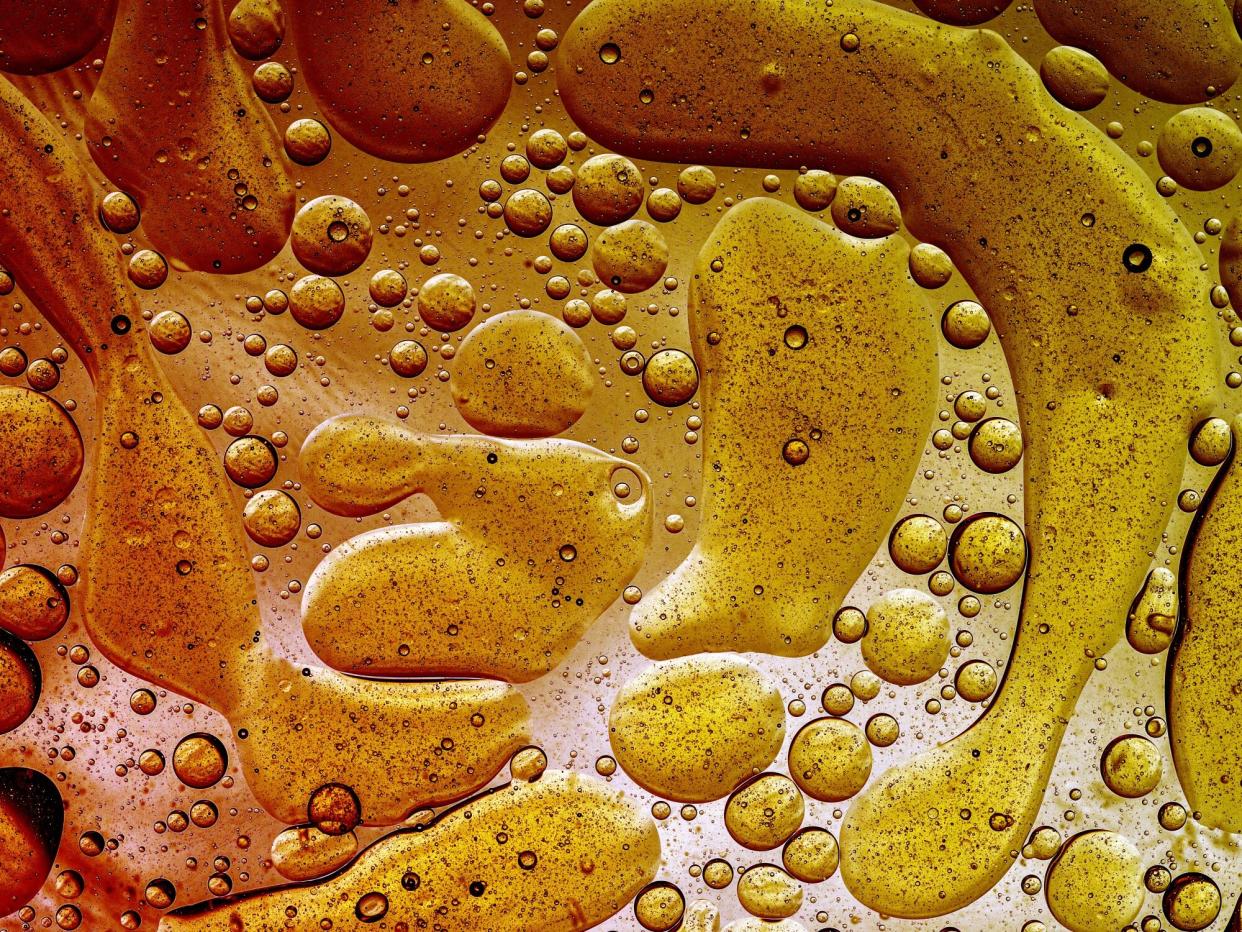 How Much Fat Should You Really Eat Every Day? , Full frame of abstract shapes and textures formed of bubbles and drops oil stains on a gold colored liquid background.