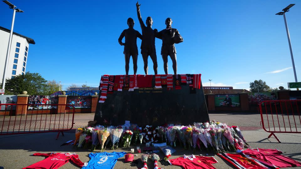 Tributes and flowers are pictured at the base of the "United Trinity" sculpture, depicting former Manchester United players George Best, Denis Law and Bobby Charlton. - Jon Super/AFP/Getty Images